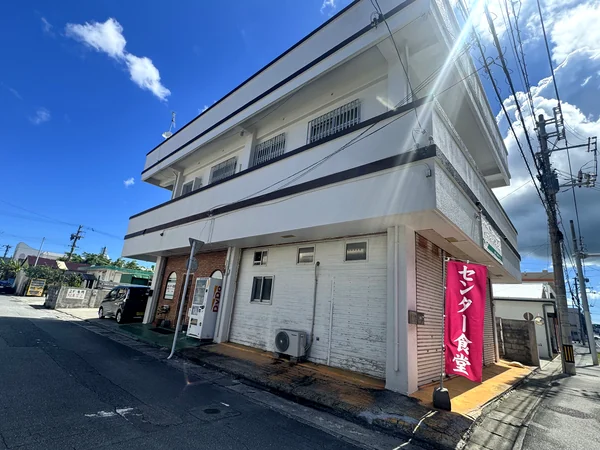 道路沿いに立つピンク色ののぼりが目印となる、糸満市センター食堂の建物外観