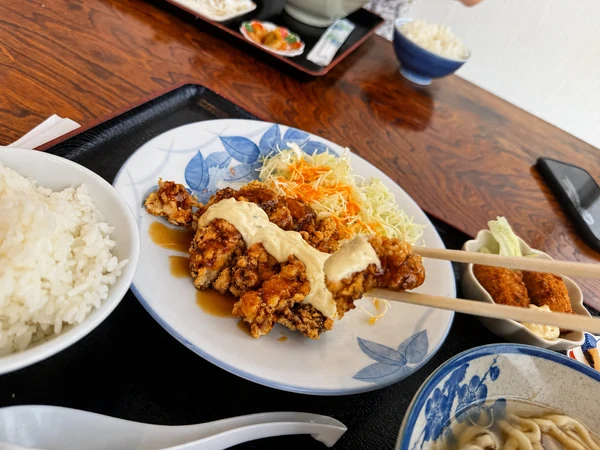 うるま市のうるまる食堂で提供されたチキン南蛮を箸で持ち上げた様子。サクサクの衣に甘めの南蛮ソースとタルタルソースがたっぷり絡んでいる
