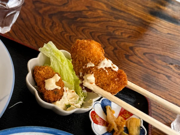 うるま市のうるまる食堂で提供されたカキフライを箸で持ち上げた様子。サクサクの衣にタルタルソースを添えた揚げたての一品